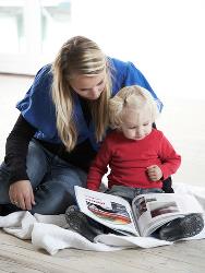 En voksen sidder på gulvet og læser højt for et barn